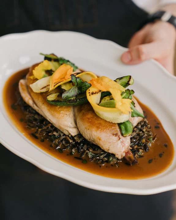 Gourmet roasted chicken on wild rice, garnished with vibrant vegetables, served on a white plate.