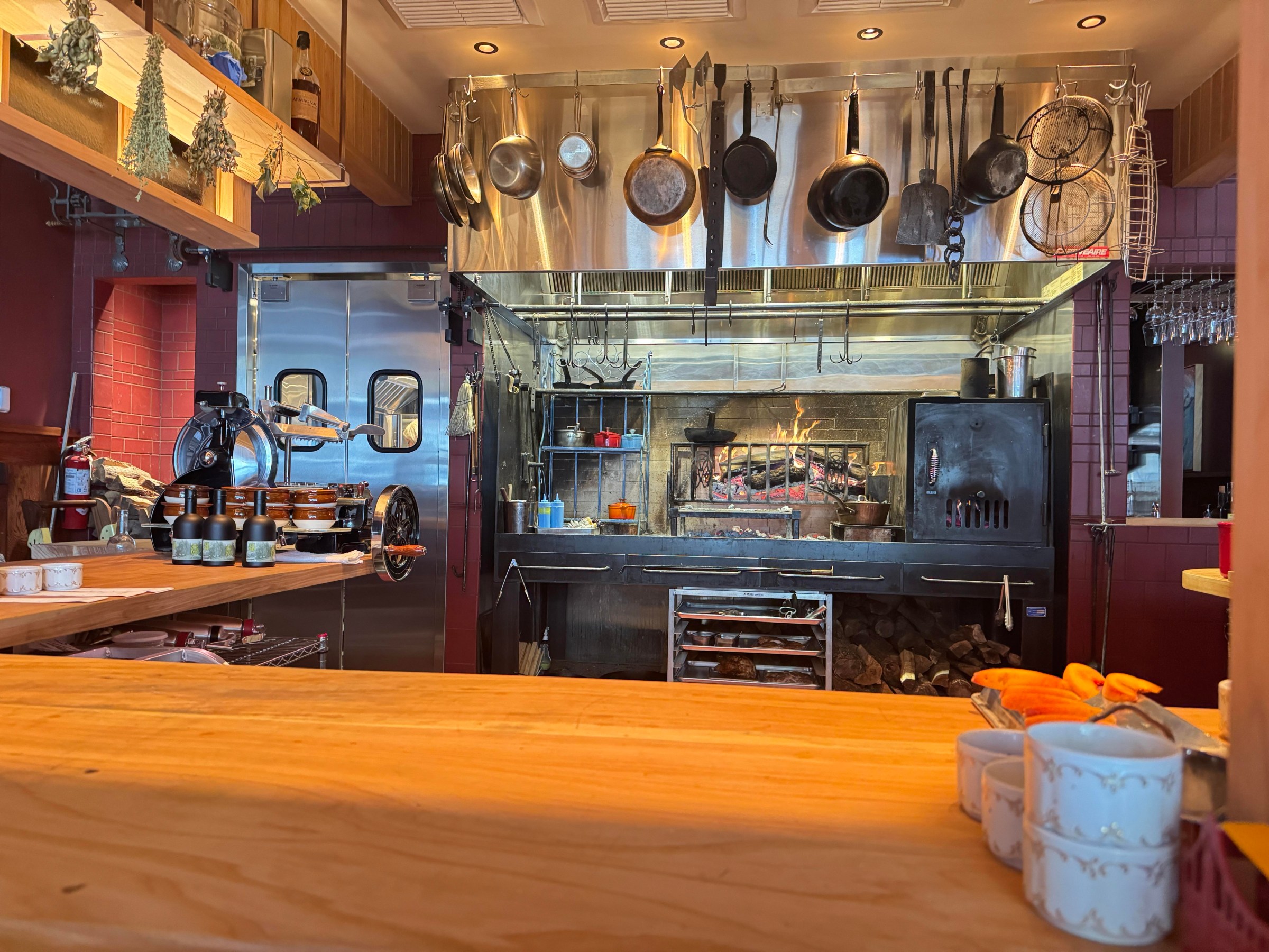 The kitchen at La Cigale in San Francisco, with wood-fired hearth and pans hanging overhead.