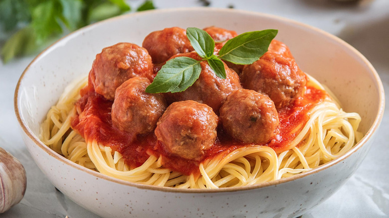 Bowl of spaghetti with meatballs in a white bowl garnished with basil