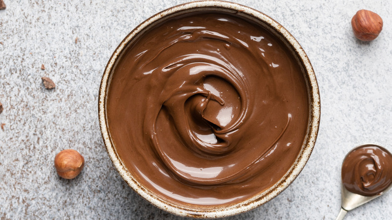 Chocolate hazelnut spread in a bowl with raw hazelnuts around the bowl