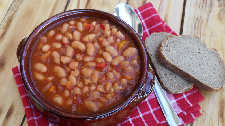 A bowl of baked beans on a red kitchen cloth with read and spoon on the side