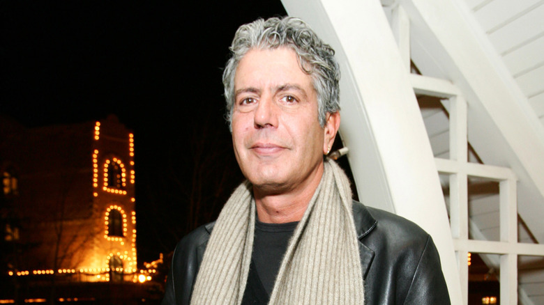 Bourdain outside swearing a leather jacket and scarf