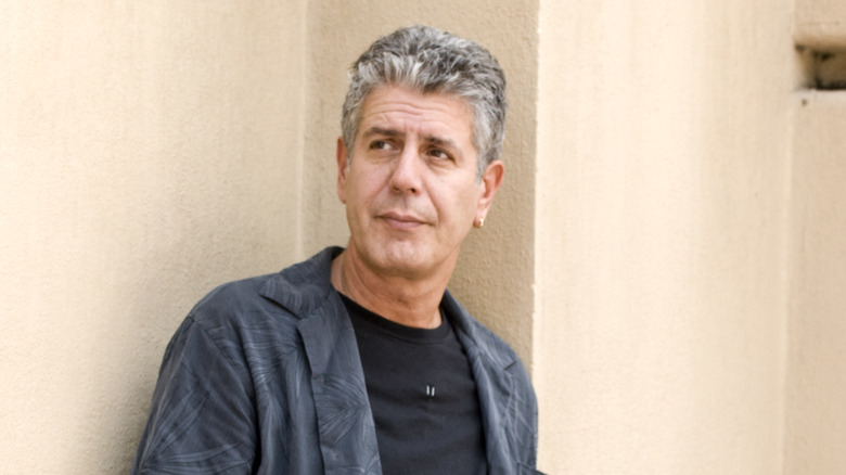Anthony Bourdain leaning against a wall in a casual outfit