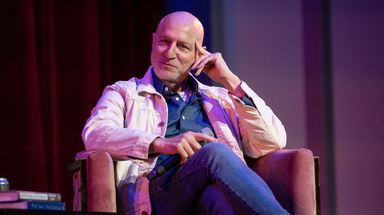 Chef Tom Colicchio sits on a chair while holding a mic onstage