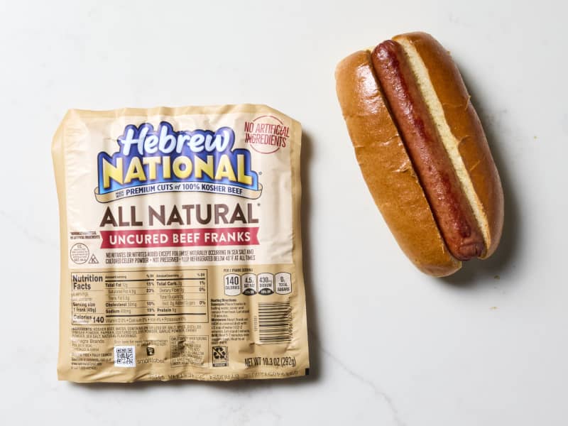 overhead shot of a package of hebrew national uncured beef hot dogs, and a cooked hot dog in a bun to the right of it.